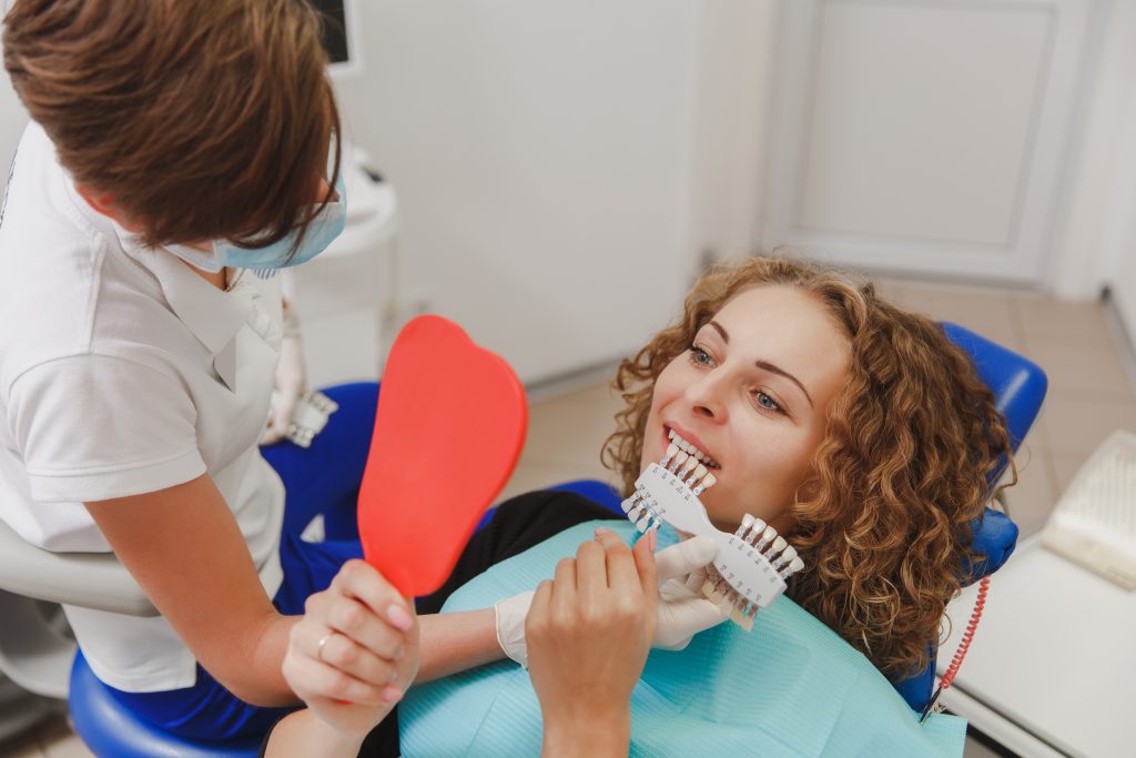 The dentist comparing patient's teeth shade with samples for bleaching treatment